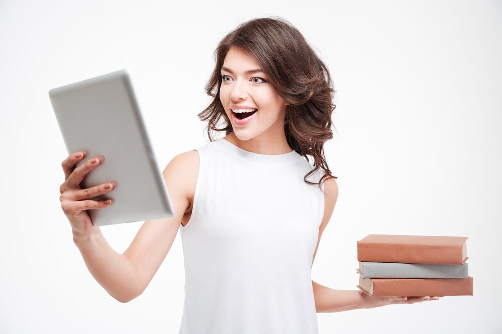 Cheerful woman choosing between tablet computer and paper books isolated on a white background